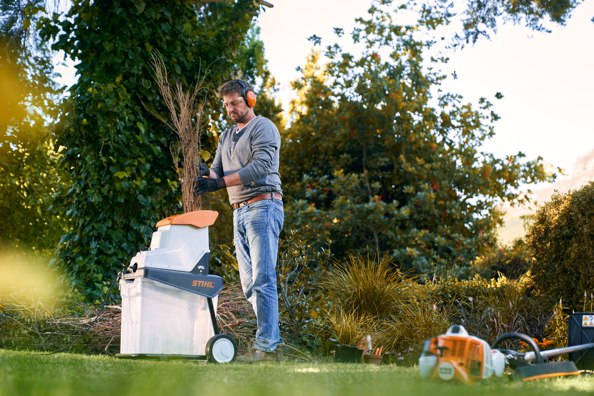 En mann med hørselvern forminsker grener før kompostering med en elektrisk kompostkvern GHE 140 fra STIHL